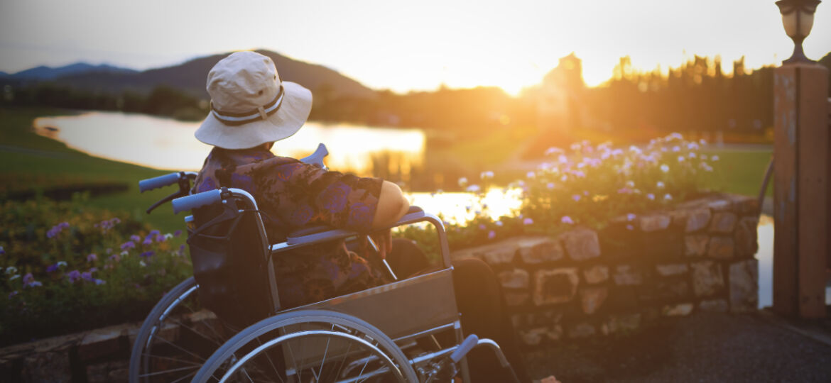 A person sitting in a wheelchair looks out into the hoizon looking out at mountains and a body of water.